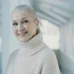 Elegant senior woman with grey hair smiling in a serene indoor setting.